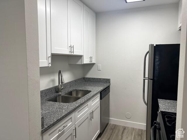 Kitchen with appliances with stainless steel finishes, white cabinetry, light hardwood / wood-style flooring, and sink