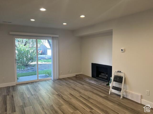 Unfurnished living room with hardwood / wood-style floors, heating unit, and a brick fireplace