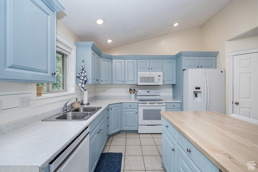 Kitchen featuring blue cabinetry, white appliances, sink, vaulted ceiling, and light tile patterned floors