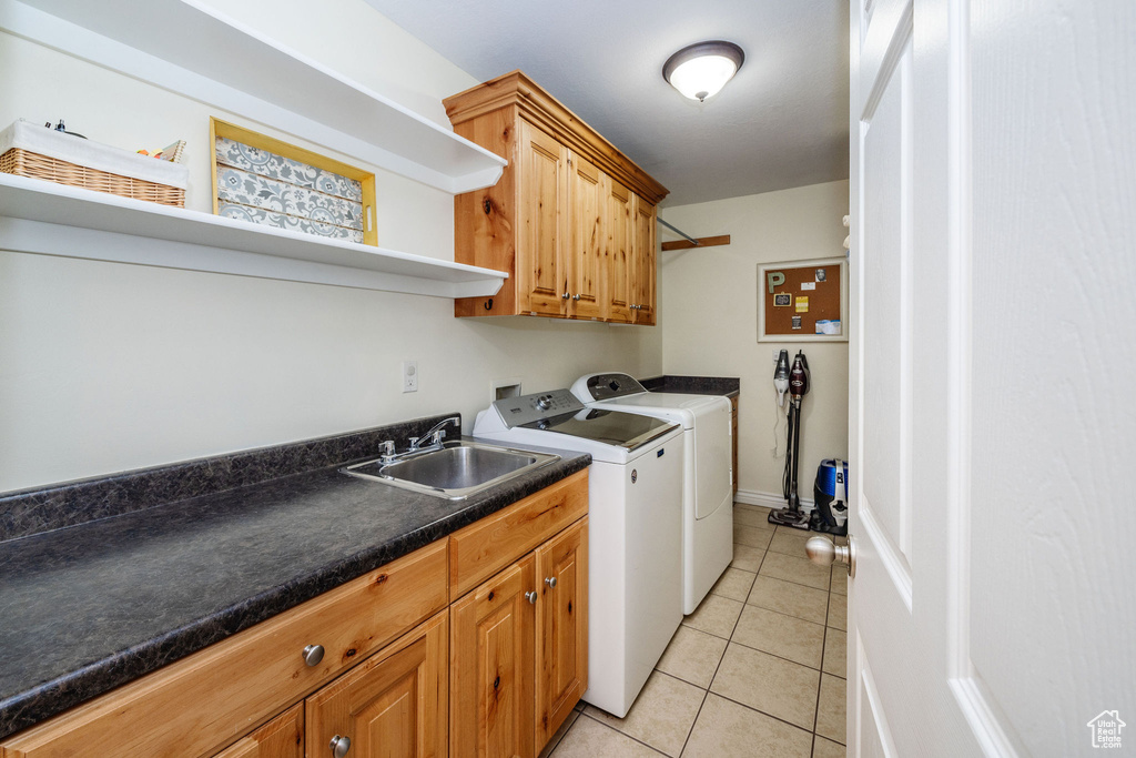 Clothes washing area featuring washer and dryer, cabinets, sink, and light tile patterned flooring