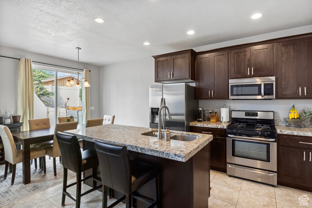 Kitchen with appliances with stainless steel finishes, light stone countertops, sink, dark brown cabinets, and an island with sink