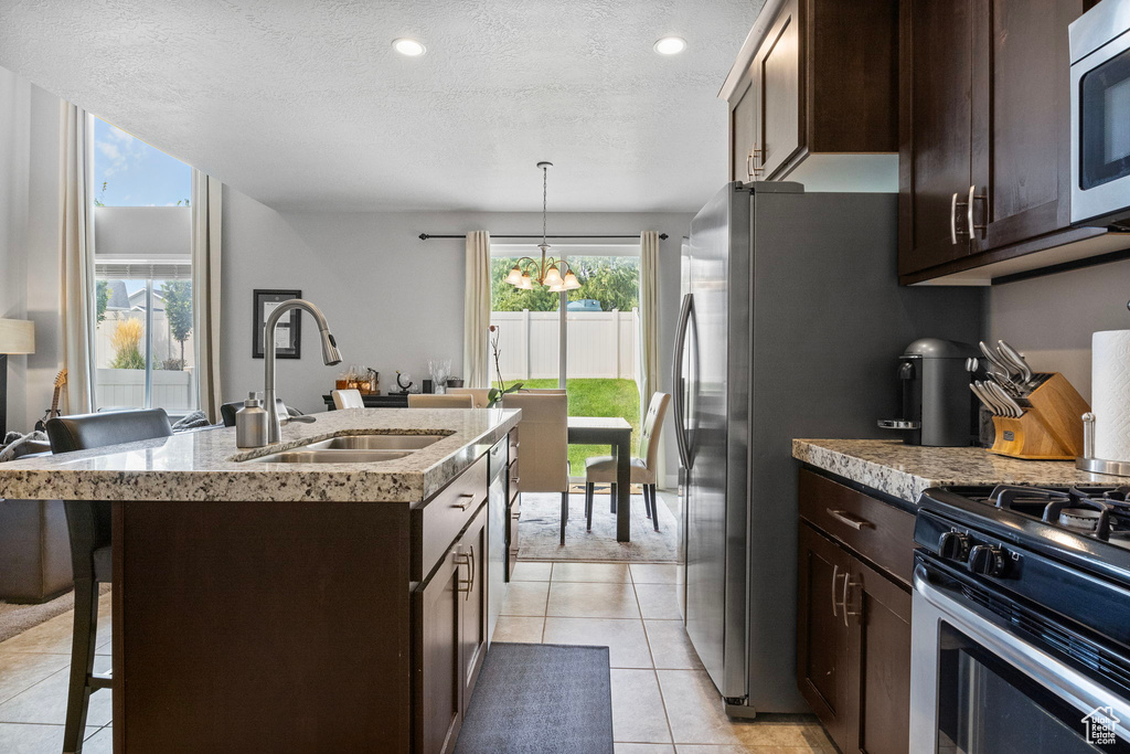 Kitchen with a textured ceiling, decorative light fixtures, an island with sink, stainless steel appliances, and sink