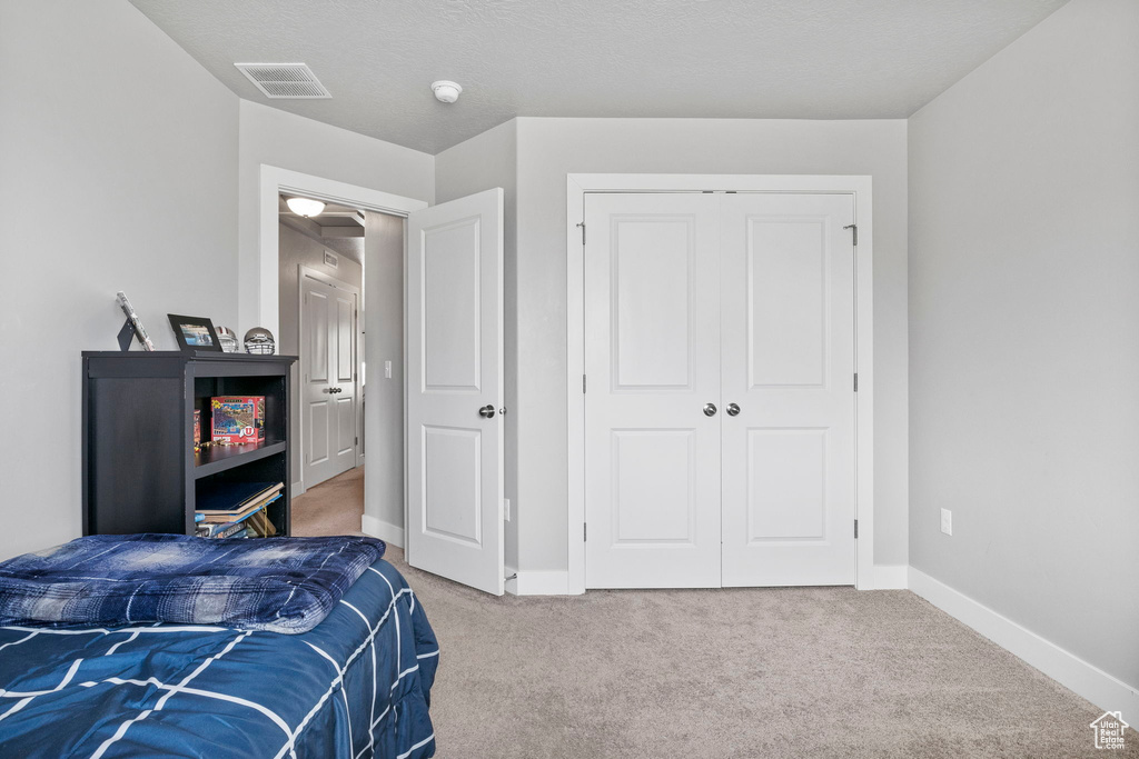 Carpeted bedroom featuring a textured ceiling and a closet