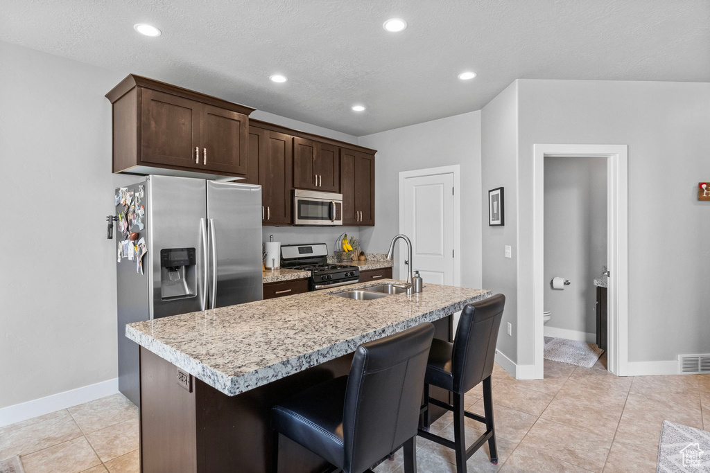 Kitchen featuring appliances with stainless steel finishes, dark brown cabinets, an island with sink, and sink