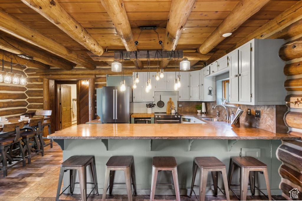 Kitchen featuring stainless steel appliances, kitchen peninsula, sink, beam ceiling, and log walls