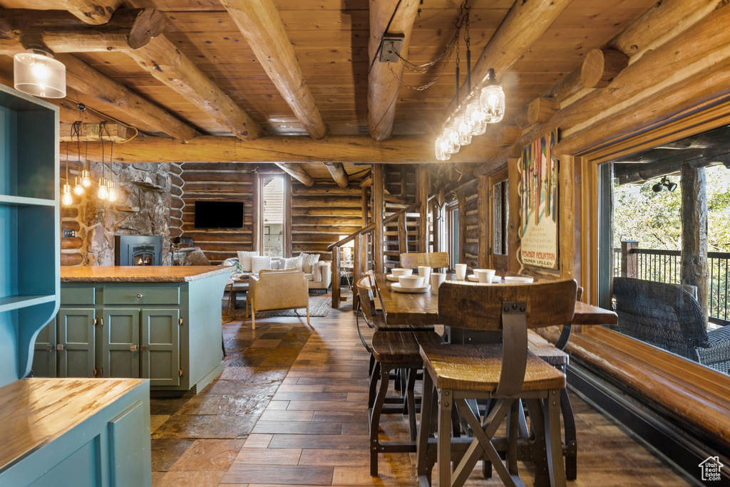 Dining area with beamed ceiling, a notable chandelier, rustic walls, dark hardwood / wood-style floors, and a stone fireplace