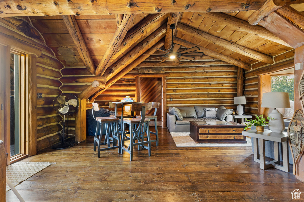 Living room with lofted ceiling with beams, wood ceiling, dark hardwood / wood-style floors, rustic walls, and ceiling fan