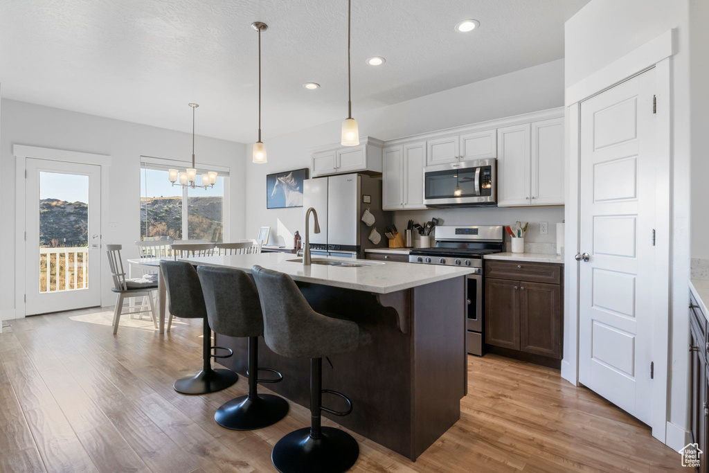 Kitchen with pendant lighting, a kitchen island with sink, light hardwood / wood-style floors, stainless steel appliances, and a chandelier