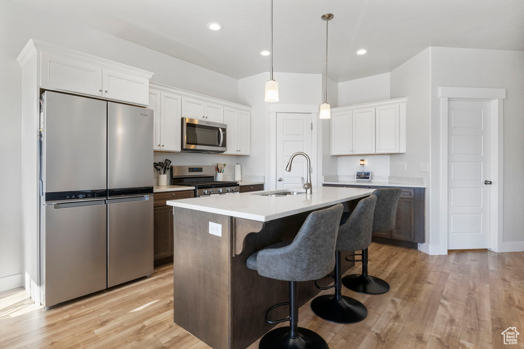 Kitchen featuring light wood-type flooring, appliances with stainless steel finishes, white cabinetry, sink, and a kitchen island with sink