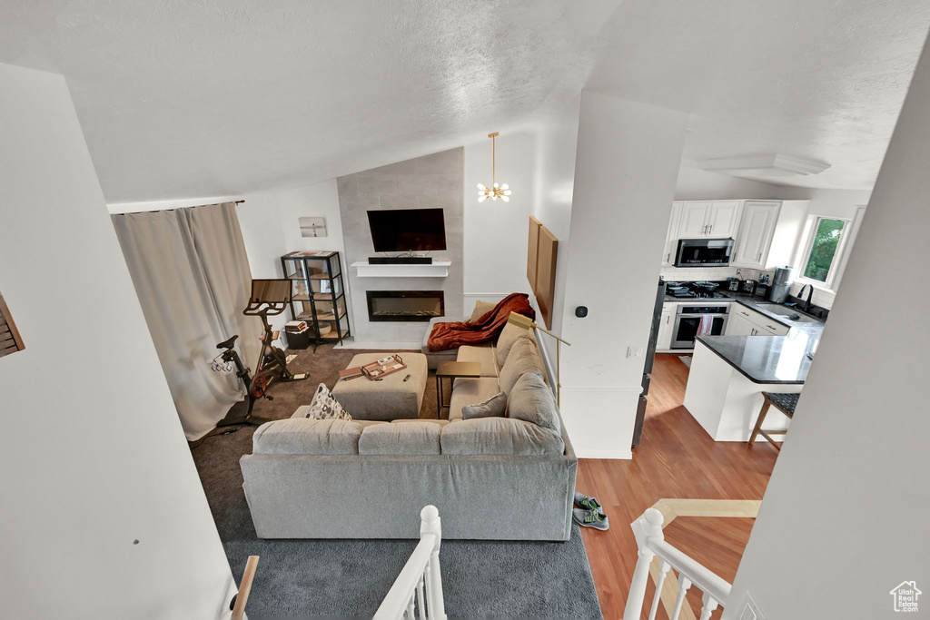 Living room featuring hardwood / wood-style floors, a textured ceiling, an inviting chandelier, sink, and lofted ceiling