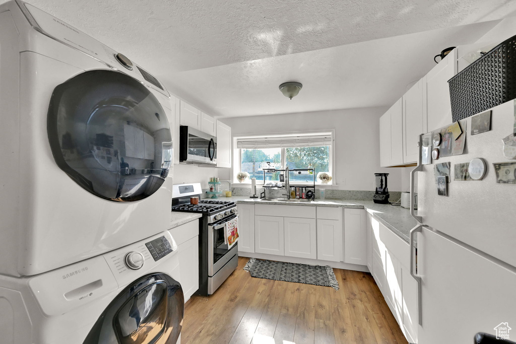 Kitchen featuring stacked washer and clothes dryer, stainless steel appliances, light wood-type flooring, and white cabinetry