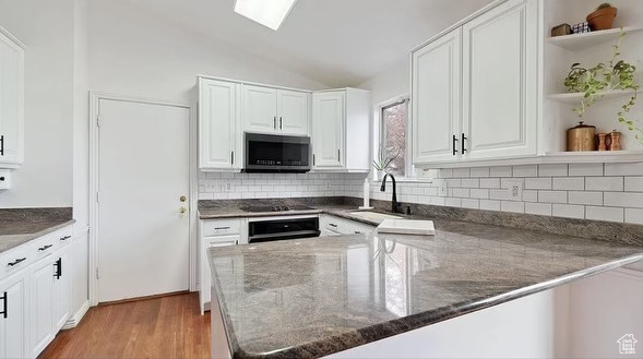 Kitchen featuring black appliances, sink, light wood-type flooring, and white cabinets