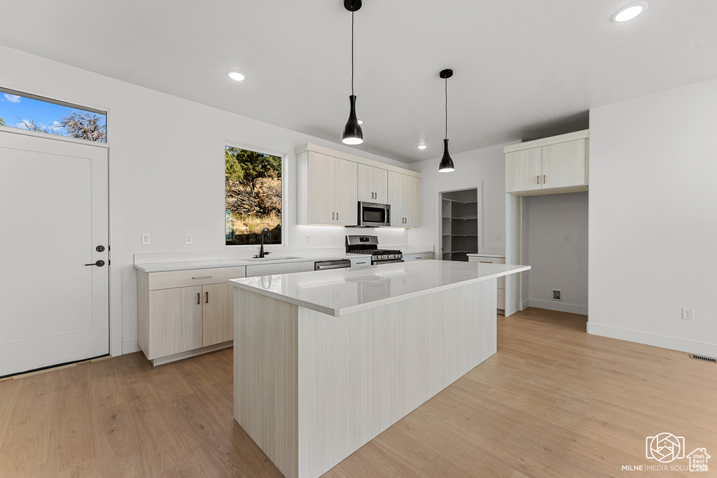 Kitchen featuring pendant lighting, light wood-type flooring, sink, a kitchen island, and stainless steel appliances