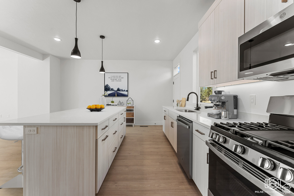 Kitchen with sink, a kitchen island, light hardwood / wood-style flooring, appliances with stainless steel finishes, and decorative light fixtures