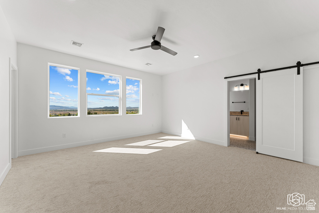 Unfurnished bedroom with ceiling fan, light colored carpet, ensuite bathroom, and a barn door