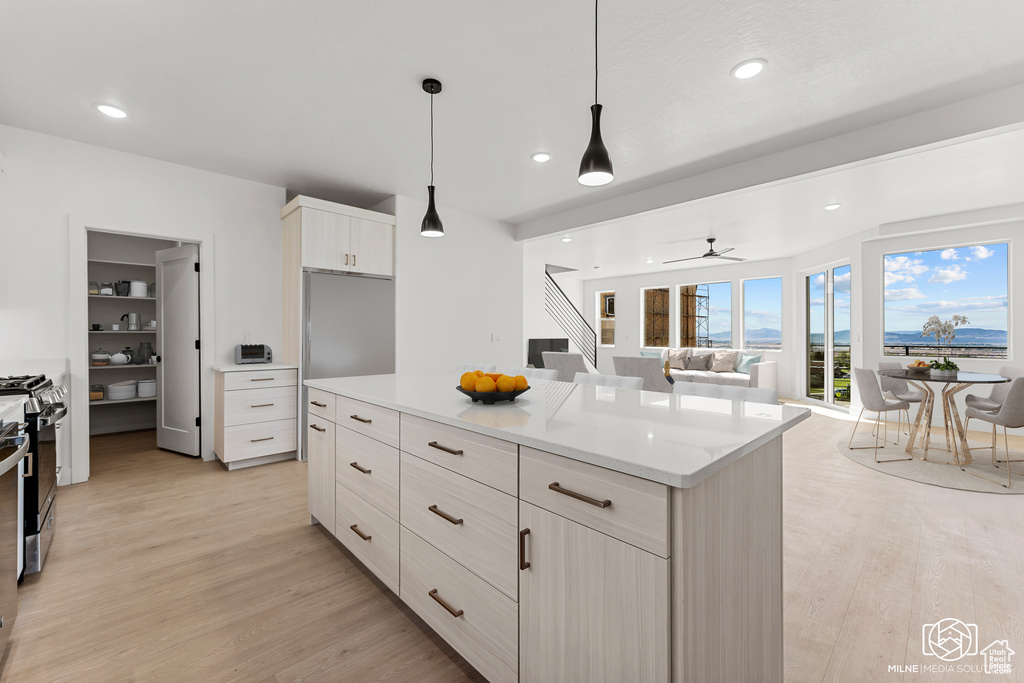 Kitchen with appliances with stainless steel finishes, hanging light fixtures, a kitchen island, ceiling fan, and light hardwood / wood-style flooring