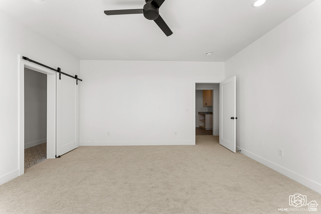 Unfurnished bedroom with light carpet, a closet, ceiling fan, and a barn door