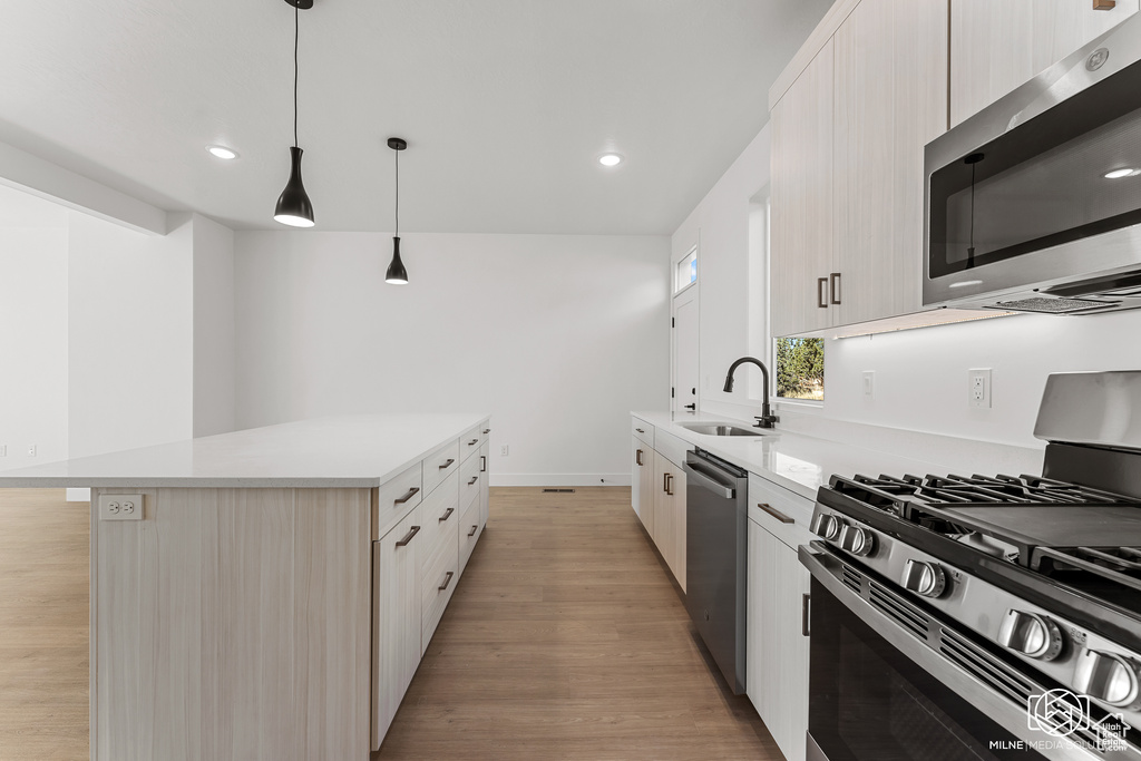 Kitchen with appliances with stainless steel finishes, a kitchen island, light wood-type flooring, decorative light fixtures, and sink