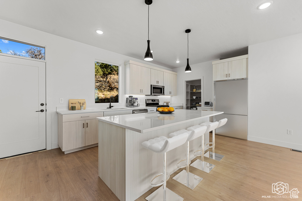 Kitchen featuring hanging light fixtures, sink, a kitchen island, light hardwood / wood-style flooring, and stainless steel appliances