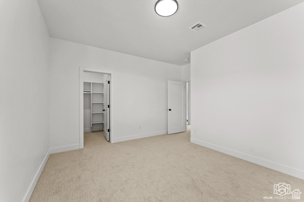 Unfurnished bedroom featuring light carpet, a closet, and a walk in closet