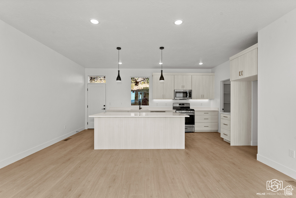 Kitchen featuring light wood-type flooring, a center island, stainless steel appliances, and decorative light fixtures