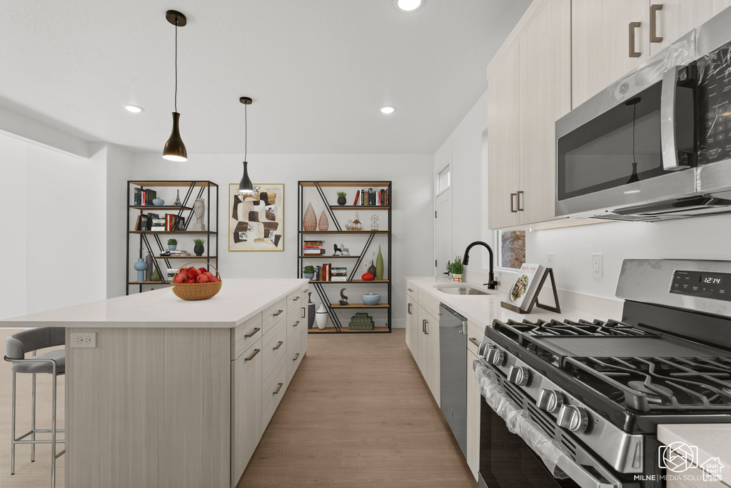 Kitchen featuring light wood-type flooring, a center island, sink, stainless steel appliances, and decorative light fixtures