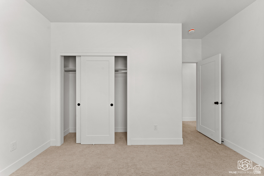 Unfurnished bedroom featuring light carpet and a closet