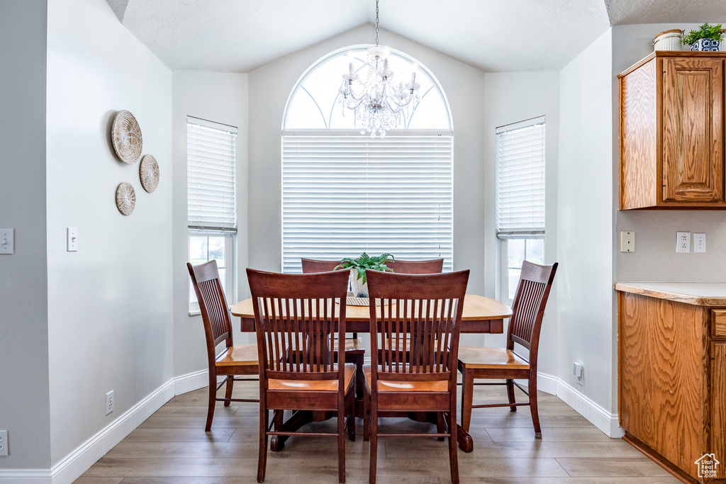 Dining area with hardwood / wood-style floors, a notable chandelier, and vaulted ceiling