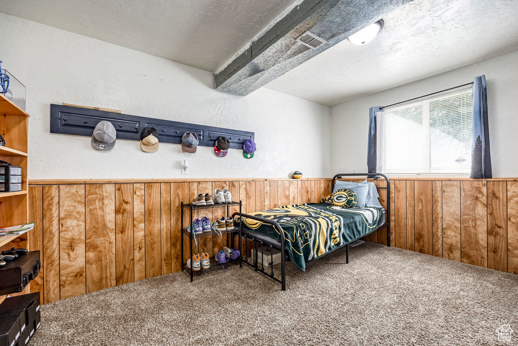 Bedroom featuring a textured ceiling, beam ceiling, wooden walls, and carpet