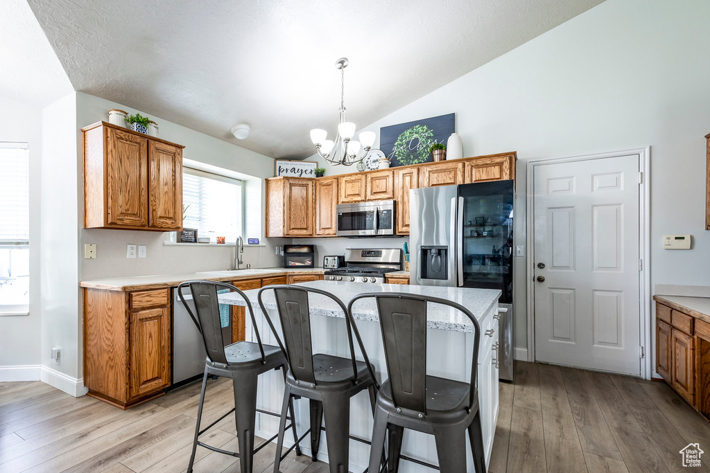 Kitchen with light hardwood / wood-style floors, hanging light fixtures, stainless steel appliances, and an inviting chandelier