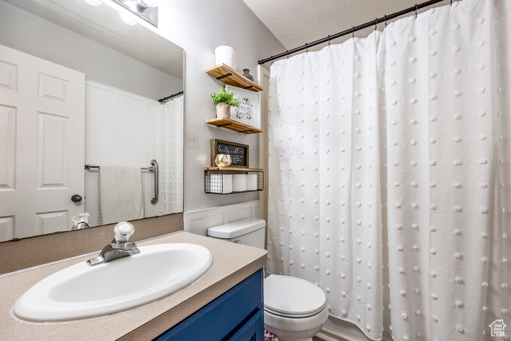 Bathroom with a textured ceiling, vanity, toilet, and a shower with shower curtain