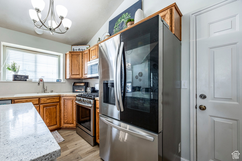 Kitchen with decorative light fixtures, a notable chandelier, light hardwood / wood-style floors, stainless steel appliances, and lofted ceiling