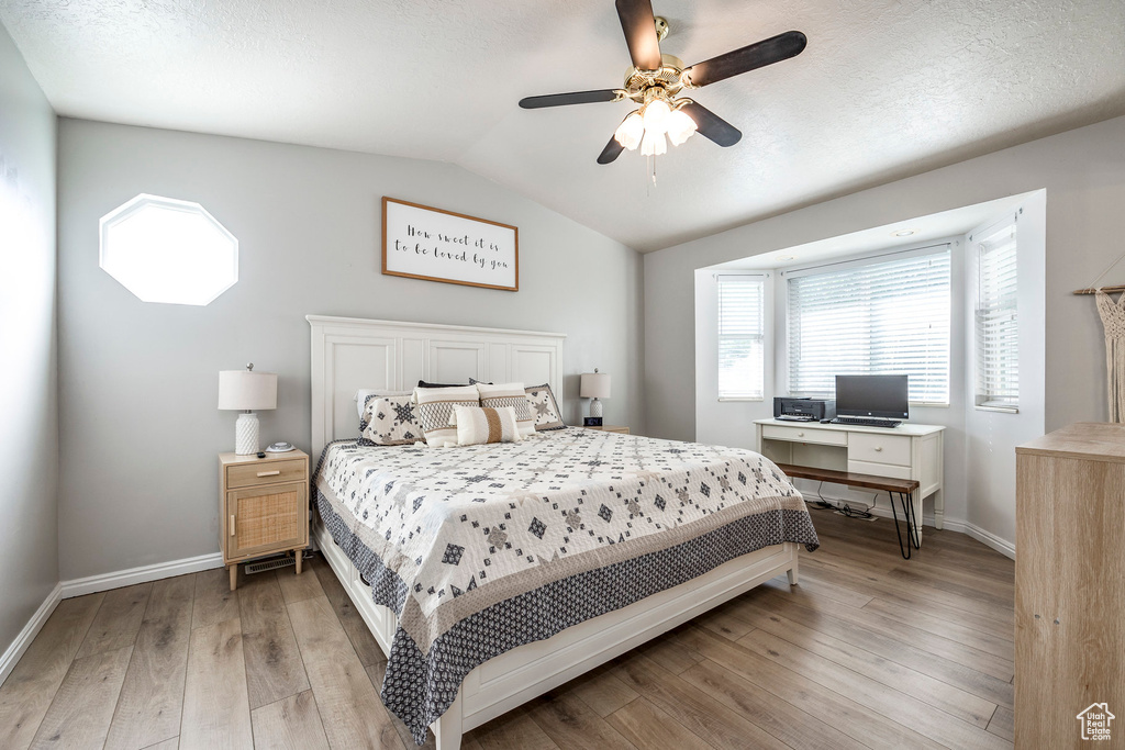 Bedroom with lofted ceiling, ceiling fan, light wood-type flooring, and a textured ceiling