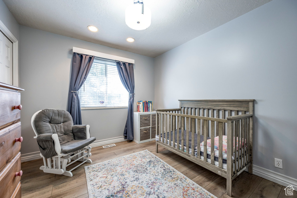 Bedroom featuring a textured ceiling, a nursery area, and hardwood / wood-style flooring