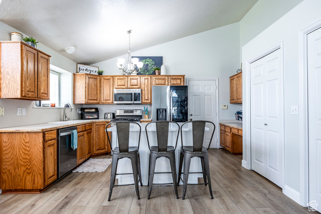 Kitchen featuring light wood-type flooring, a notable chandelier, stainless steel appliances, hanging light fixtures, and vaulted ceiling