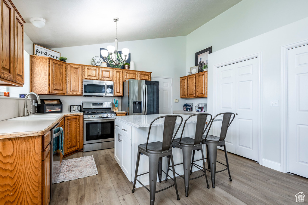 Kitchen with light wood-type flooring, decorative light fixtures, stainless steel appliances, a center island, and an inviting chandelier