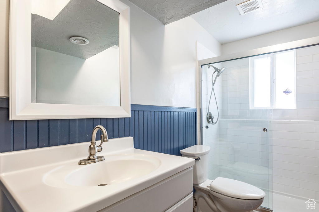 Bathroom with toilet, a shower with door, a textured ceiling, and vanity