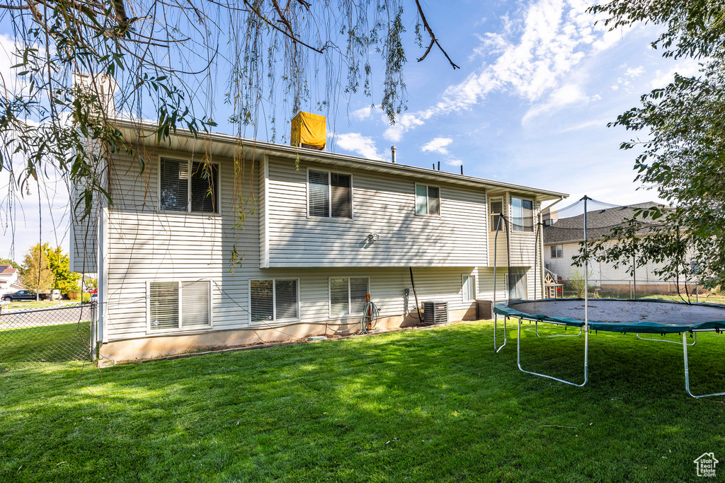 Back of property with central AC unit, a lawn, and a trampoline