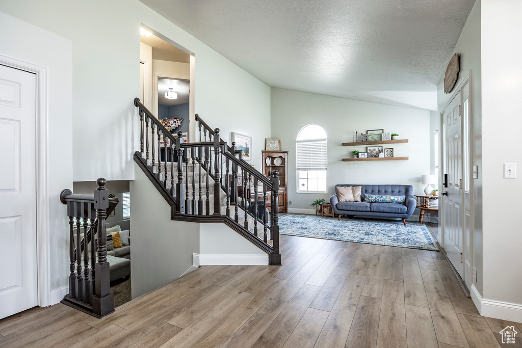 Entrance foyer with lofted ceiling, light hardwood / wood-style floors, and a textured ceiling