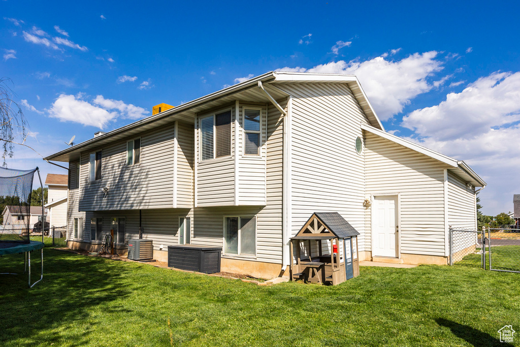 Back of house with cooling unit, a lawn, and a trampoline