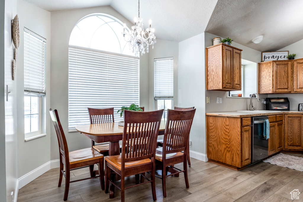 Dining space with lofted ceiling, a chandelier, sink, and light hardwood / wood-style floors