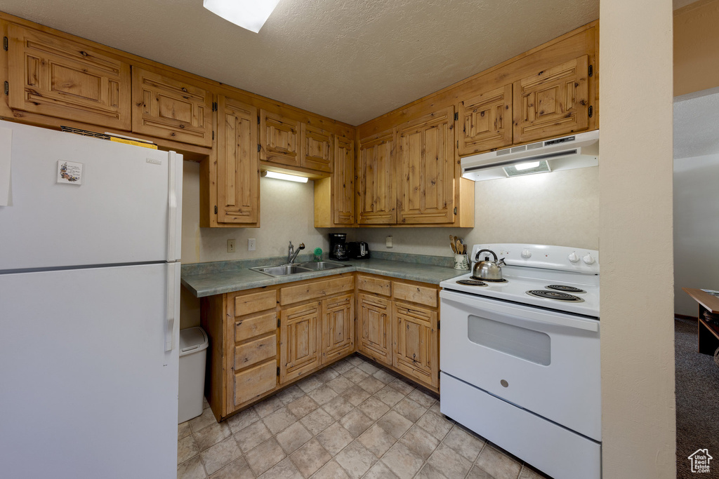 Kitchen with light countertops, under cabinet range hood, a sink, and white appliances