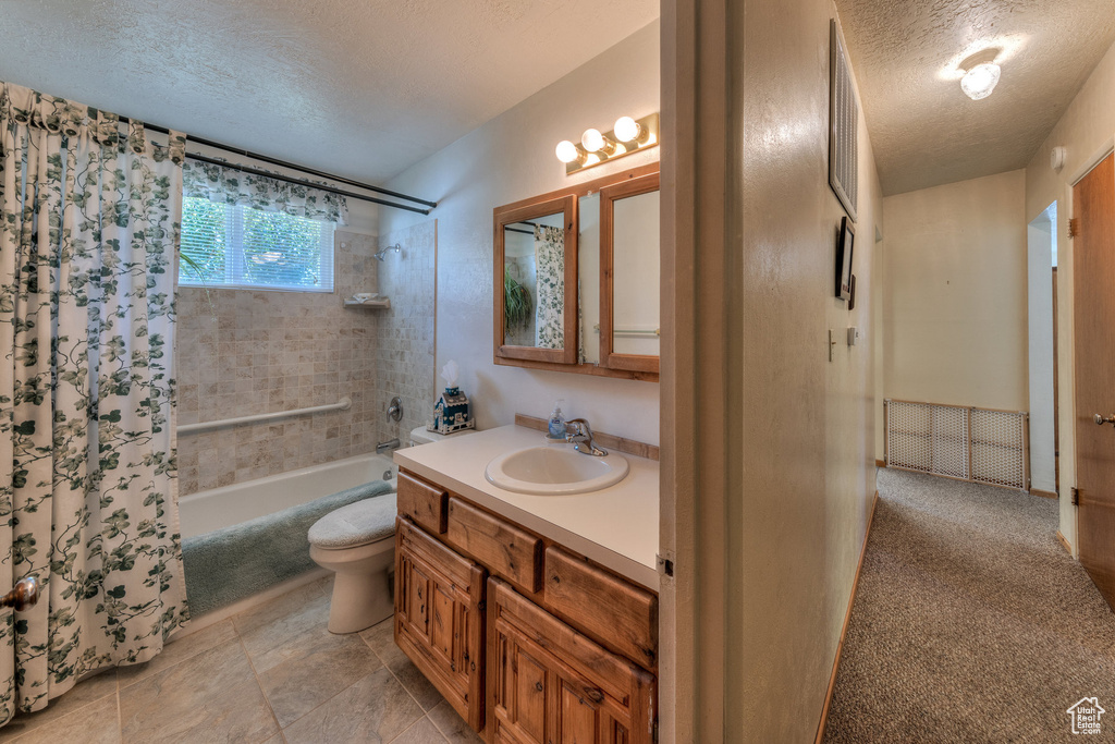 Bathroom with shower / bath combo with shower curtain, vanity, a textured ceiling, and toilet