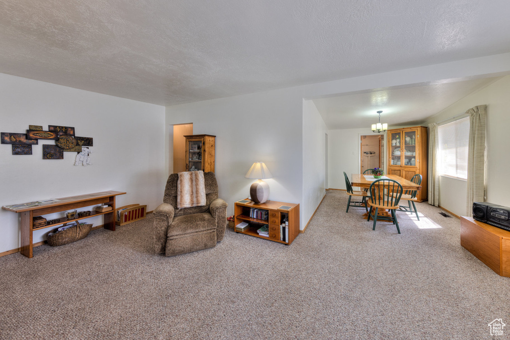 Carpeted living room with baseboards, a textured ceiling, a notable chandelier, and visible vents