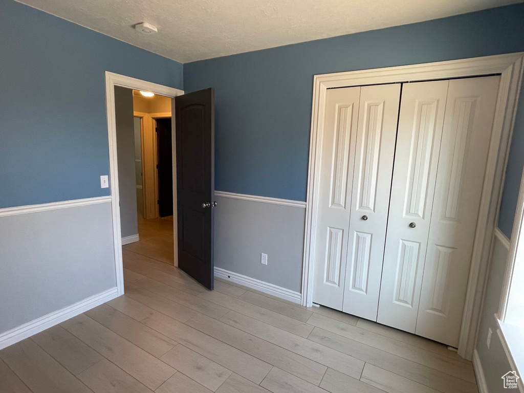 Unfurnished bedroom featuring a textured ceiling, light hardwood / wood-style flooring, and a closet