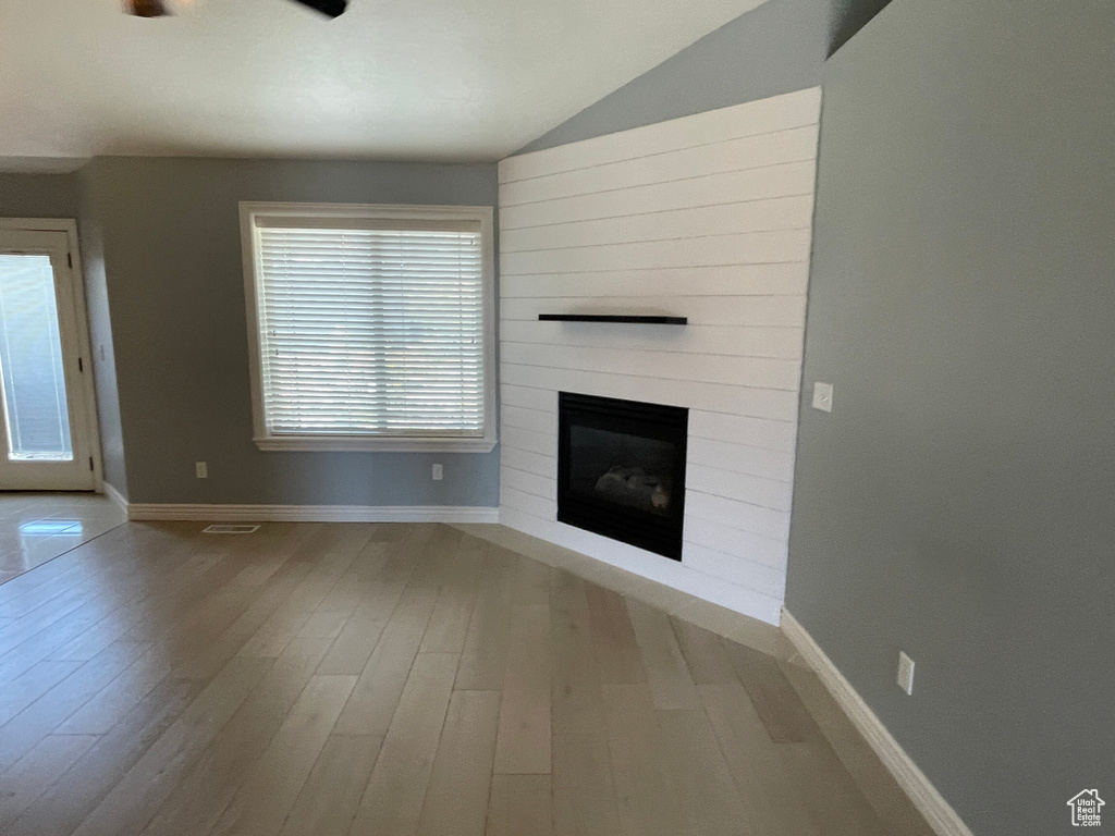 Unfurnished living room featuring hardwood / wood-style flooring, lofted ceiling, plenty of natural light, and a large fireplace