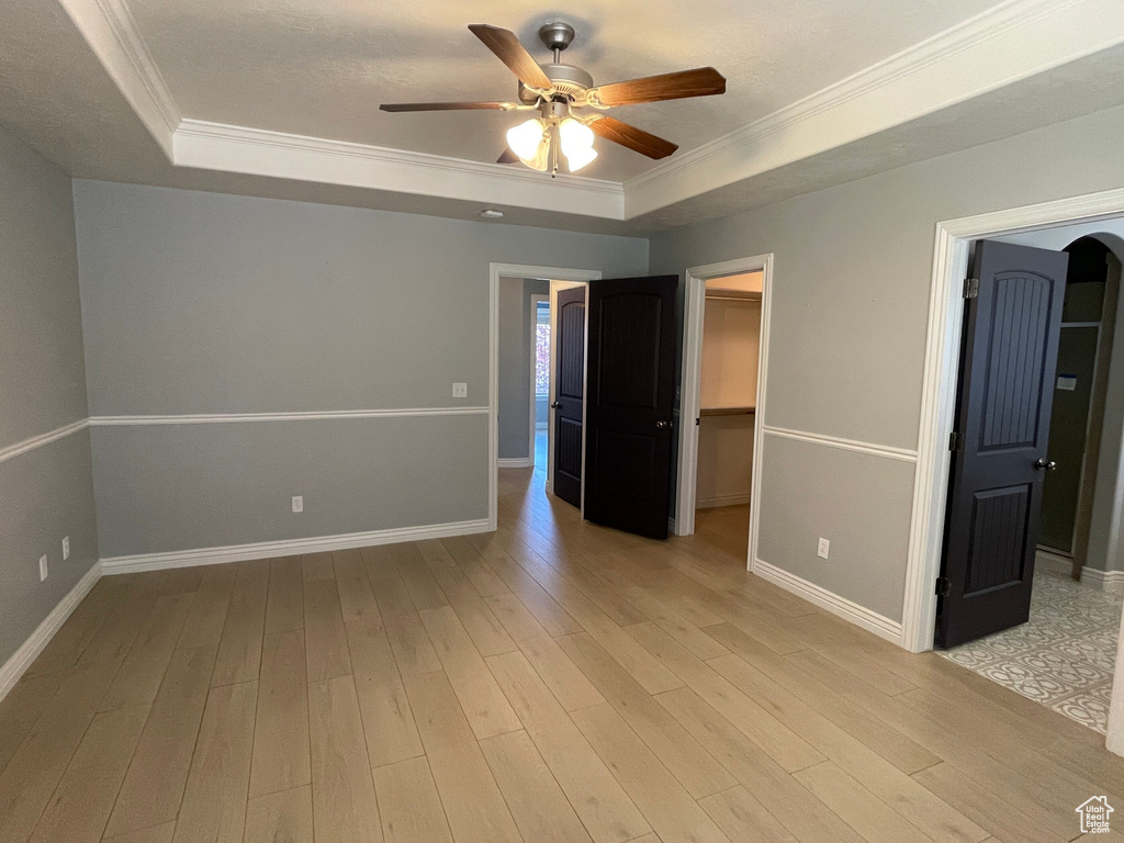 Unfurnished bedroom featuring a walk in closet, light hardwood / wood-style flooring, a closet, ornamental molding, and ceiling fan