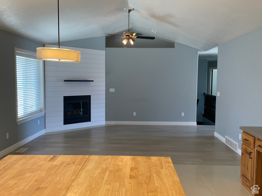 Unfurnished living room featuring dark wood-type flooring, ceiling fan, vaulted ceiling, and a fireplace