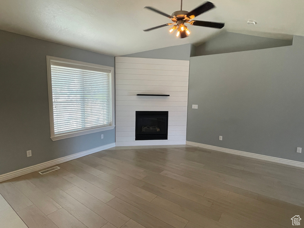 Unfurnished living room featuring lofted ceiling, ceiling fan, a fireplace, and light hardwood / wood-style flooring