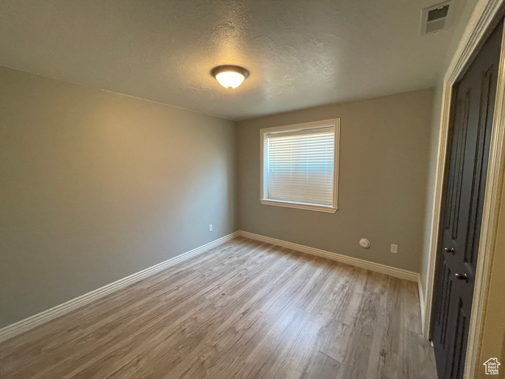 Empty room featuring light wood-type flooring and a textured ceiling